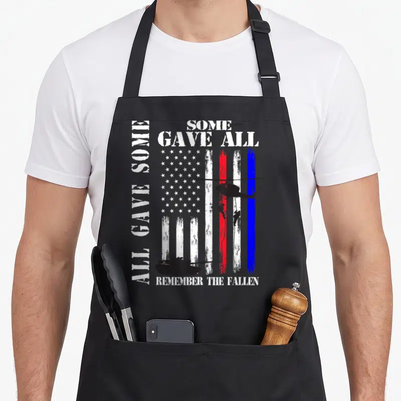 Gave family aprons - Distressed USA flag with helicopter soldiers tank and All Gave Some Some Gave All Remember — shown on a black cotton canvas apron against a white background