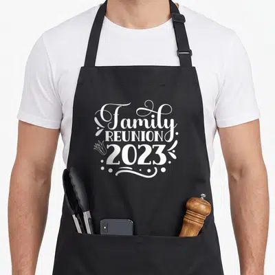 Meeting gathering apron - White stacked text reading Family Reunion 2023 with swirls and a flower icon — shown on a black cotton canvas apron against a white background