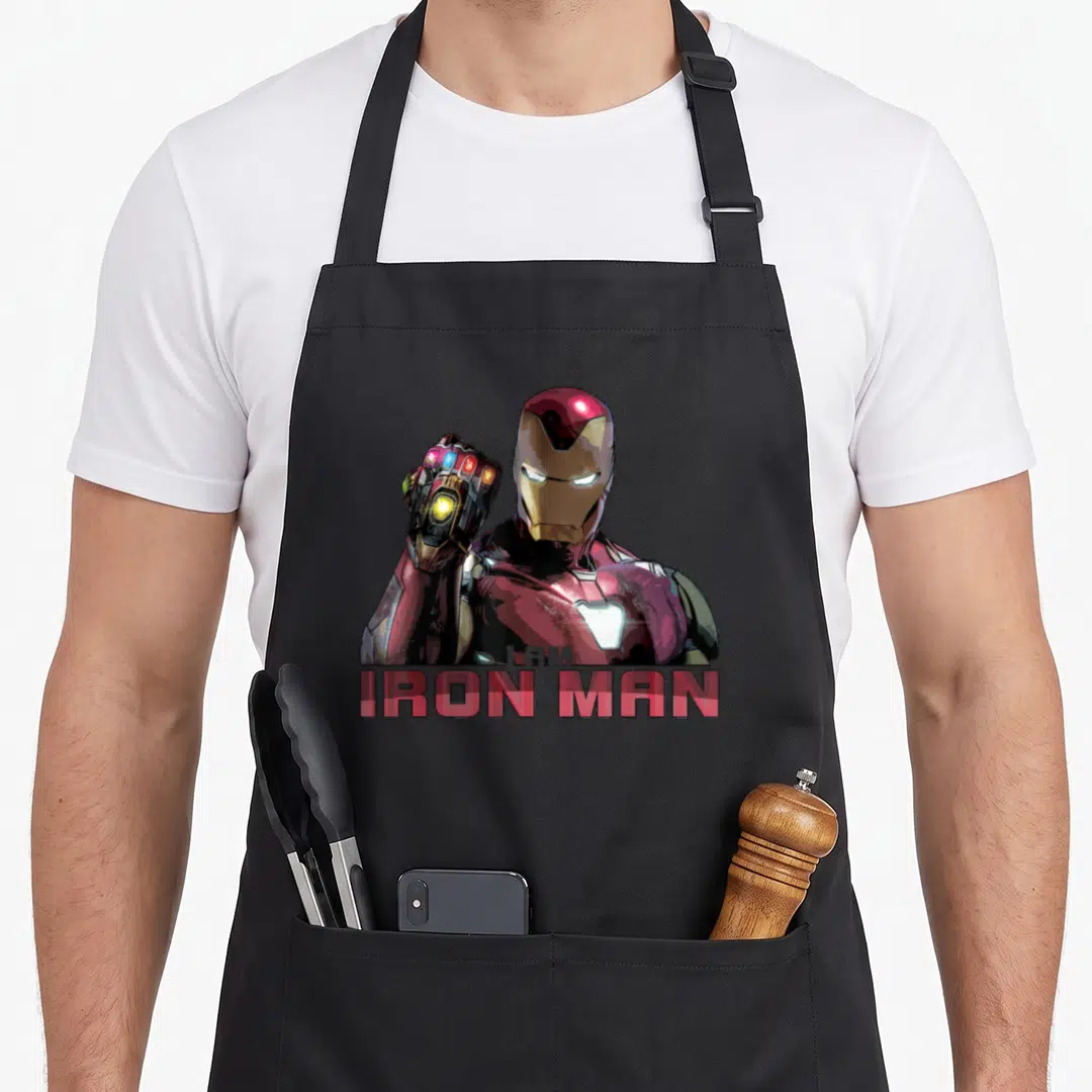 Movie ironman apron - Iron Man portrait with raised gauntlet and I AM IRON MAN text in red gold white — shown on a black cotton canvas apron against a white background