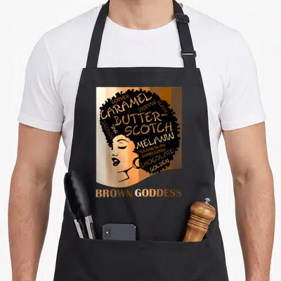 Goddess beautiful apron - Woman profile with afro filled with skin tone words and Brown Goddess text below — shown on a black cotton canvas apron against a white background