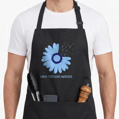 January daisy apron - Light blue daisy with dark center, flying butterflies, and awareness text below — shown on a black cotton canvas apron against a white background