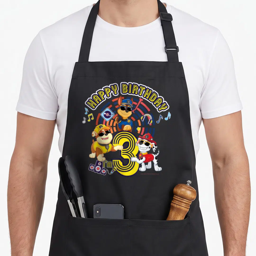 Funny age birthday apron - Three cartoon puppies with sunglasses surround yellow number 3 and I'm 3 text with music — shown on a black cotton canvas apron against a white background
