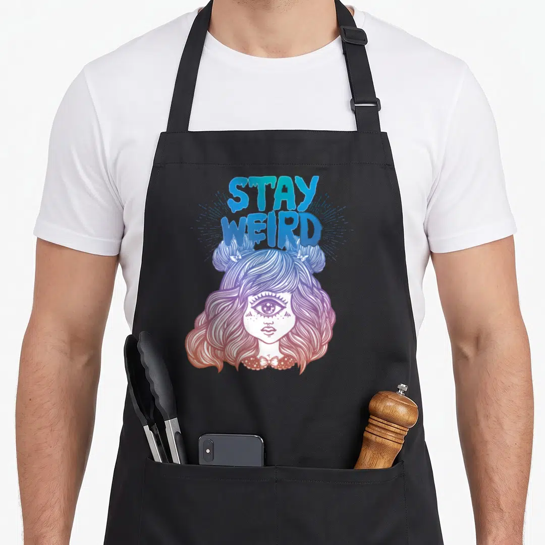 Alien weird aprons - STAY WEIRD text above girl with third eye in blue purple pink orange line art — shown on a black cotton canvas apron against a white background