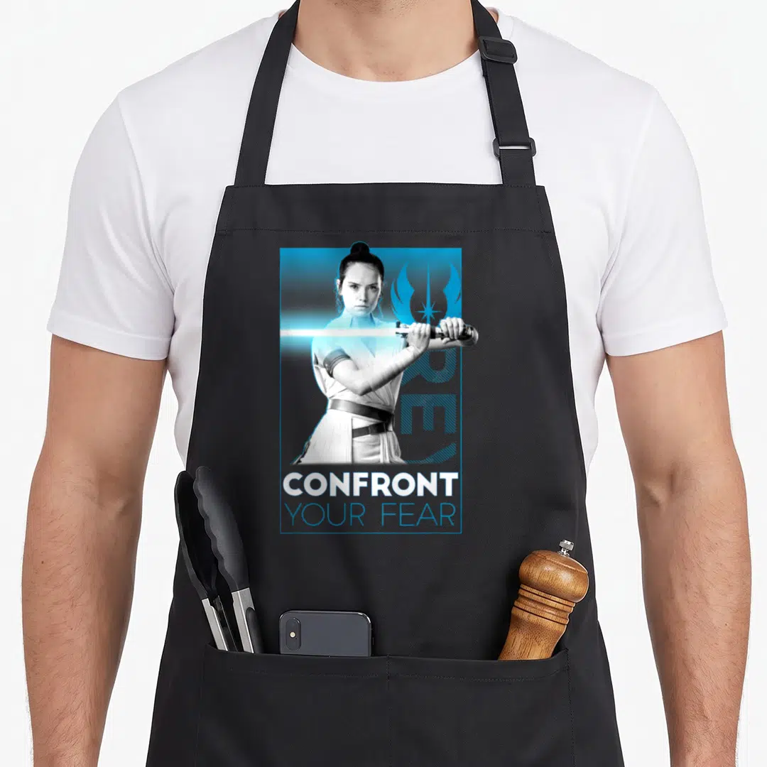Rise fear apron - Confront Your Fear text below grayscale woman holding blue lightsaber on blue background — shown on a black cotton canvas apron against a white background