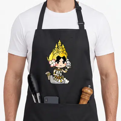 Adorable beauty apron - Chibi Thai dancer in gold crown and white robe with pink flower accent — shown on a black cotton canvas apron against a white background