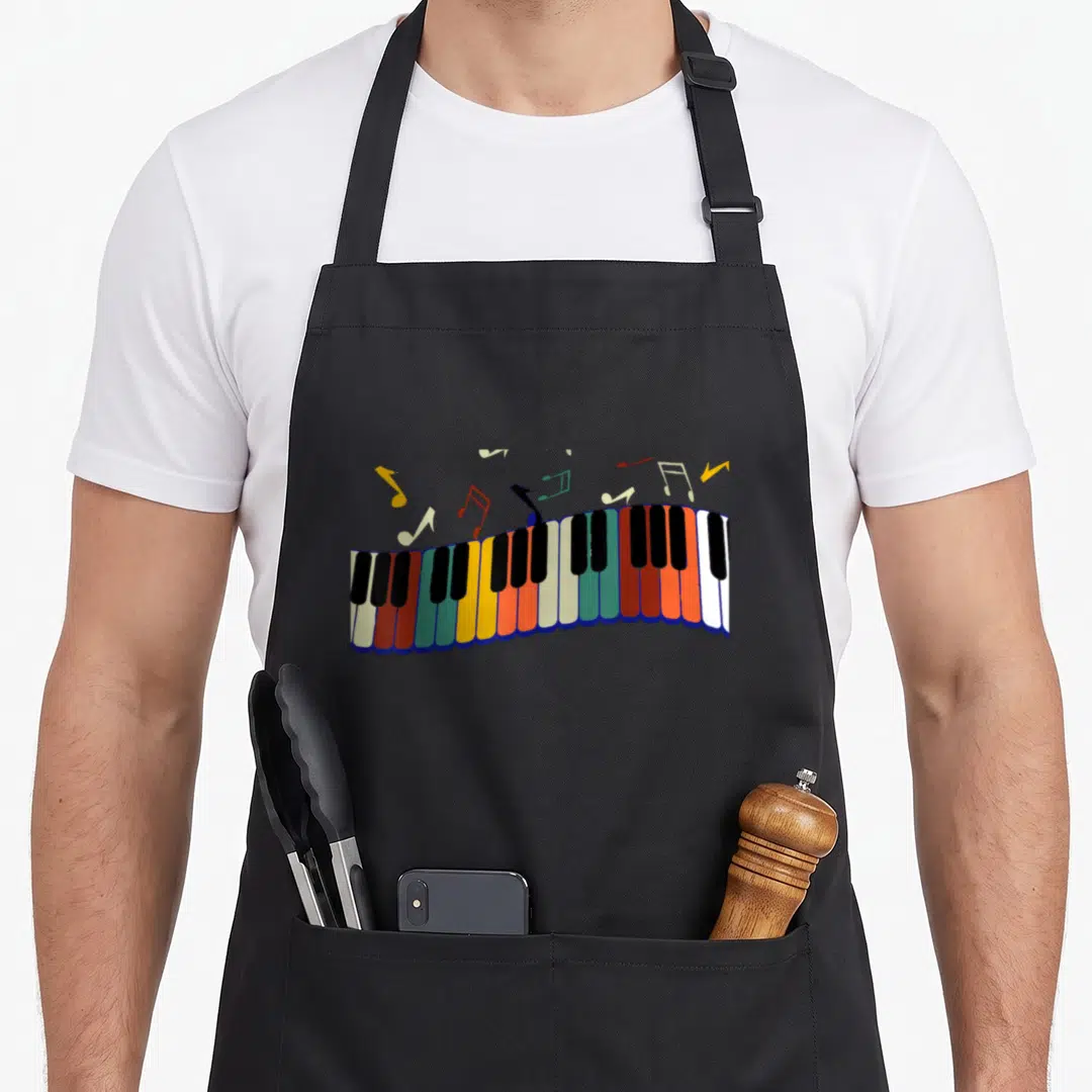 Player piano apron - Cartoon rainbow piano keyboard with floating red yellow blue green and white musical notes — shown on a black cotton canvas apron against a white background