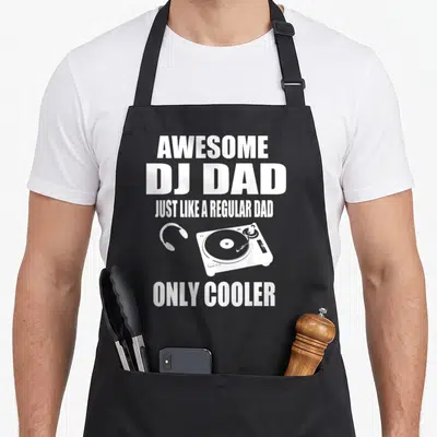 Player funny wedding aprons - White DJ Dad text stacked around turntable and headphones graphic — shown on a black cotton canvas apron against a white background