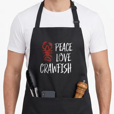 Peace crawfish boil apron - Red distressed crawfish graphic next to stacked white peace love crawfish text — shown on a black cotton canvas apron against a white background