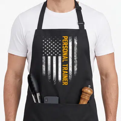 Flag personal apron - Vertical yellow PERSONAL TRAINER text overlaid on a distressed white USA flag pattern — shown on a black cotton canvas apron against a white background