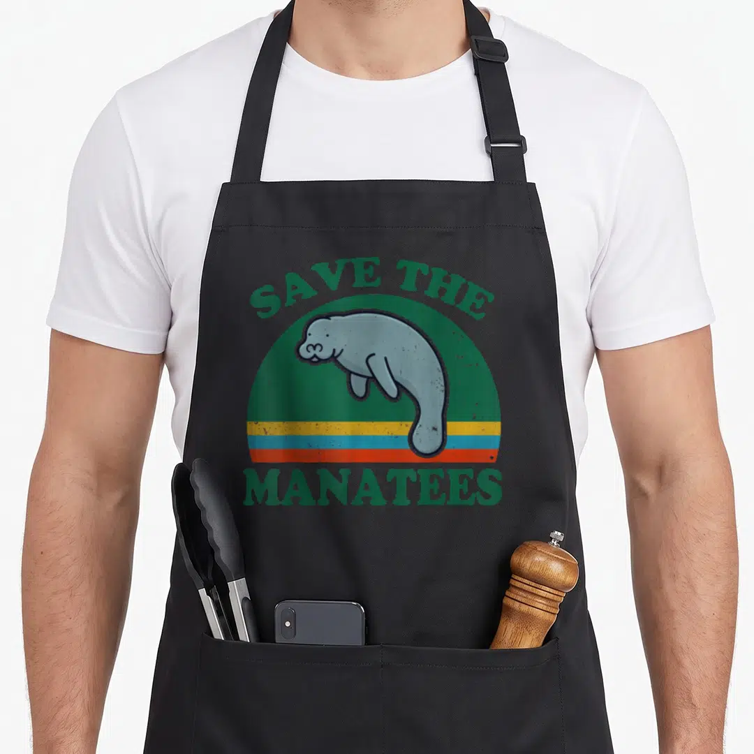 Manatee save mermaid apron - Retro SAVE THE MANATEES text above grey-blue manatee in green and striped semi-circle — shown on a black cotton canvas apron against a white background