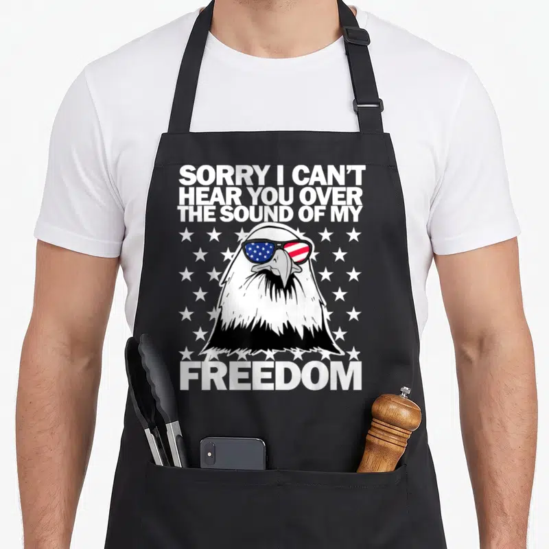 Hear i love my eagle apron - Bald eagle head wearing sunglasses with US flag lenses surrounded by white stars and bold — shown on a black cotton canvas apron against a white background