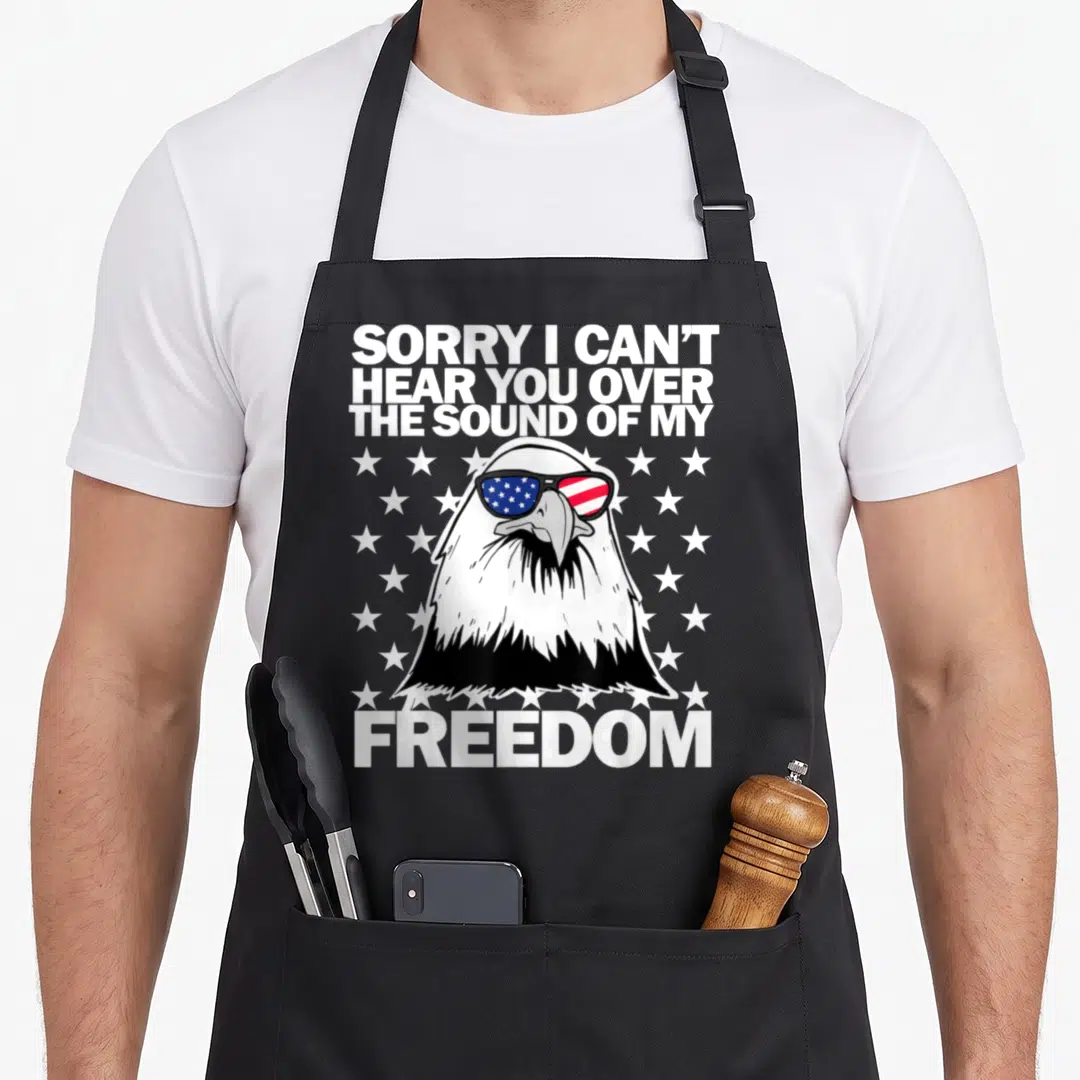 Hear i love my eagle apron - Bald eagle head wearing sunglasses with US flag lenses surrounded by white stars and bold — shown on a black cotton canvas apron against a white background