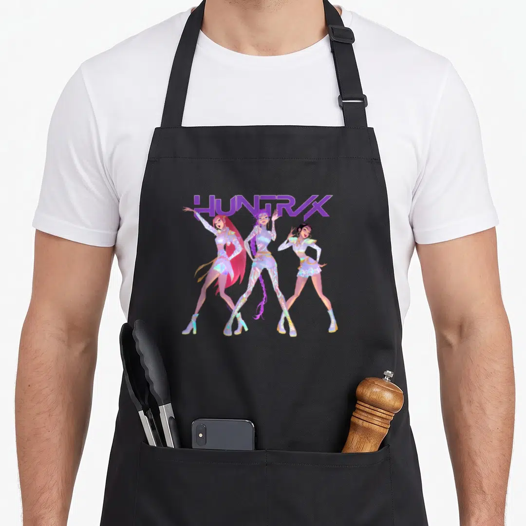 Cute huntr x apron - Three women standing in a row under HUNTRX text in purple and pink — shown on a black cotton canvas apron against a white background