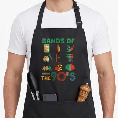 Music popular aprons - Grid of distressed icons including corn and nail under BANDS OF THE 90'S text — shown on a black cotton canvas apron against a white background