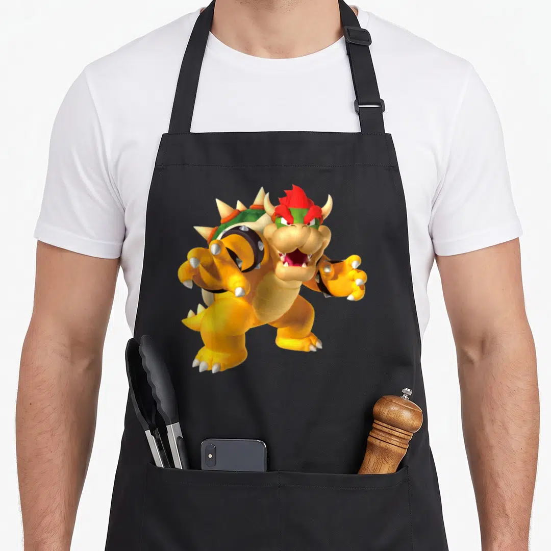 Funny poster holiday apron - 3D cartoon turtle monster with red hair, green shell, and yellow scales centered on fabric — shown on a black cotton canvas apron against a white background