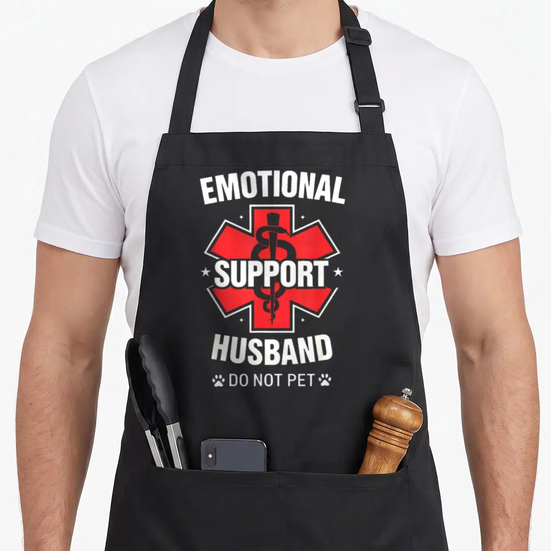 Retro emotional husband apron - Red medical cross with grey caduceus, white stacked text, and paw prints flanging — shown on a black cotton canvas apron against a white background