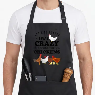 Honest chicken apron - Text LET'S BE HONEST I WAS CRAZY BEFORE THE CHICKENS with cartoon chickens and chicks — shown on a black cotton canvas apron against a white background