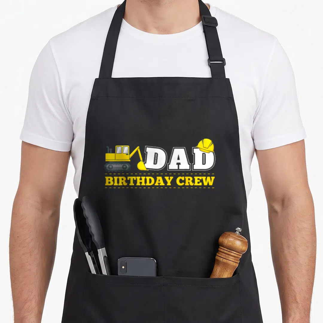 Crew daddy apron - Cartoon excavator and hard hat next to DAD BIRTHDAY CREW text — shown on a black cotton canvas apron against a white background