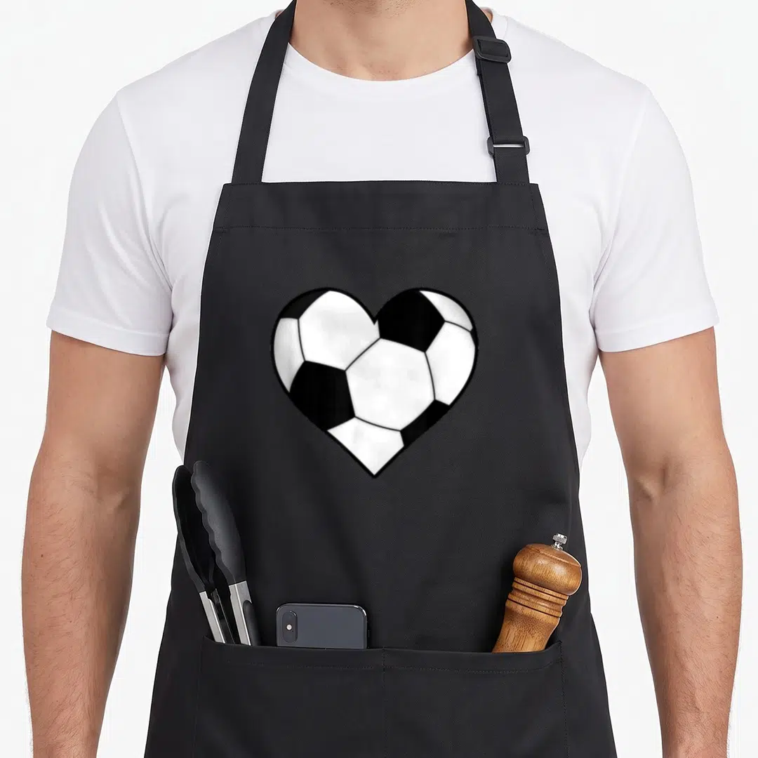 Funny soccer ball apron - Heart shaped soccer ball pattern in white and black cartoon style — shown on a black cotton canvas apron against a white background