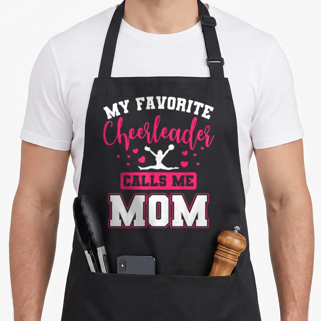Call cheerleading apron - White and pink text reading My Favorite Cheerleader Calls Me Mom with a jumping silhouette — shown on a black cotton canvas apron against a white background