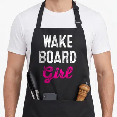 Wakeboard wakeboarding life apron - Stacked white WAKE BOARD text above pink script Girl typography — shown on a black cotton canvas apron against a white background