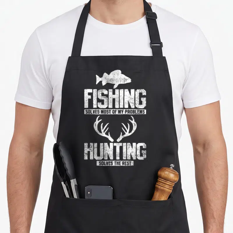 Cute hunting fishing apron - White fish silhouette and antlers with distressed text reading fishing solves most — shown on a black cotton canvas apron against a white background