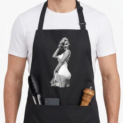 Beach marilyn monroe apron - Black and white photo of Marilyn Monroe in a white swimsuit holding a towel — shown on a black cotton canvas apron against a white background