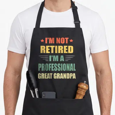 Cute retired professional apron - Stacked text reading I'm Not Retired I'm A Professional Great Grandpa with red stars — shown on a black cotton canvas apron against a white background