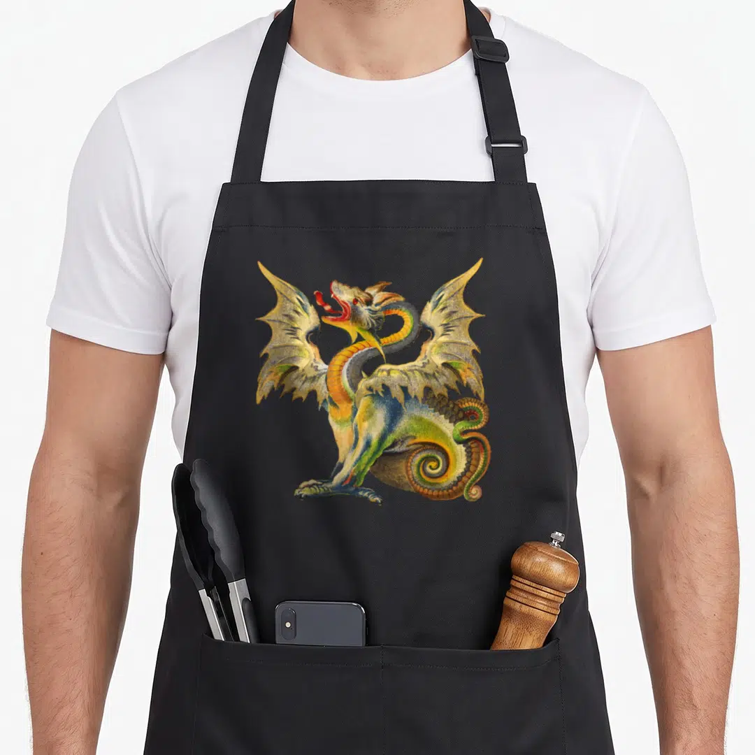 Mythical renaissance apron - Realistic dragon illustration in green, yellow, and blue centered on fabric — shown on a black cotton canvas apron against a white background