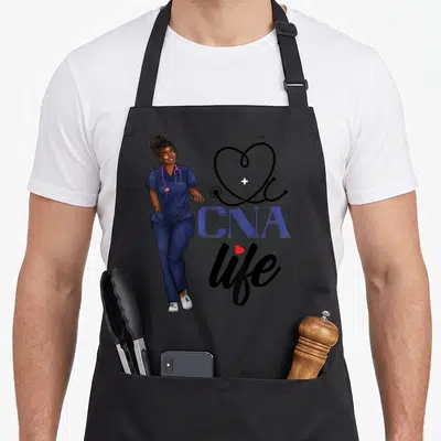 Cna african american aprons - Cartoon woman in navy scrubs beside stethoscope heart and CNA life text — shown on a black cotton canvas apron against a white background