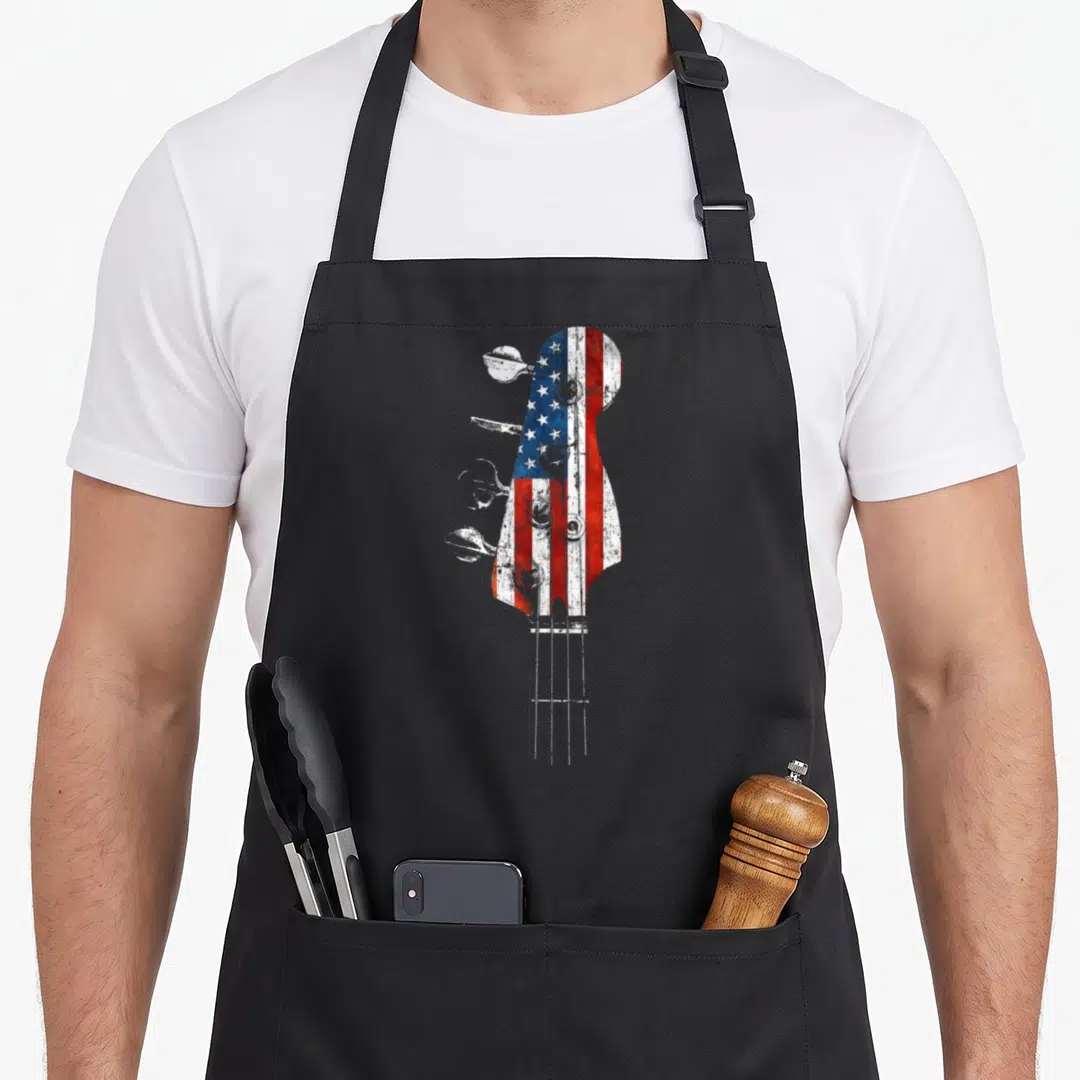 Bass usa flag apron - Distressed bass guitar headstock filled with red white and blue flag pattern — shown on a black cotton canvas apron against a white background
