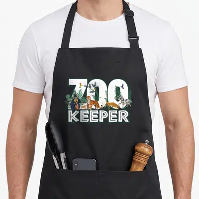 Zookeeper wood apron - ZOO KEEPER text with cartoon tiger zebra monkey birds and plants in white green orange black — shown on a black cotton canvas apron against a white background