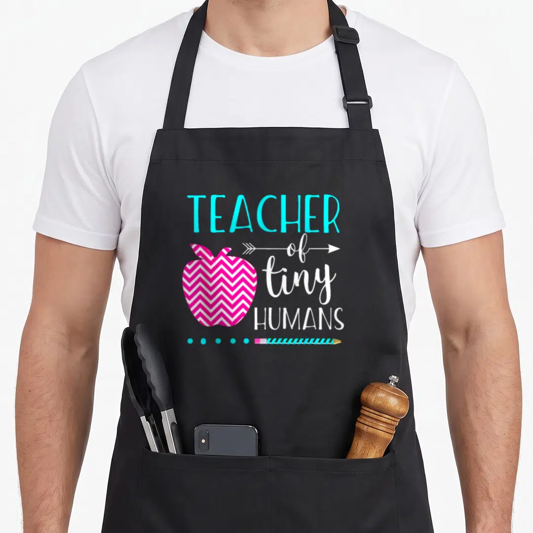 Tiny kindergarten teacher apron - Pink chevron apple next to TEACHER of tiny HUMANS text with cyan pencil and dots — shown on a black cotton canvas apron against a white background