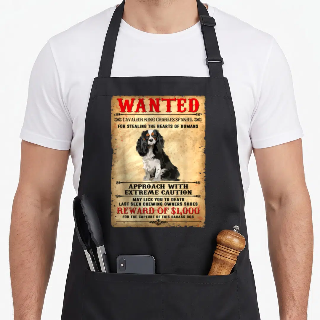 Charle spaniel dog king apron - Distressed wanted poster of a seated Cavalier King Charles Spaniel with humorous text — shown on a black cotton canvas apron against a white background