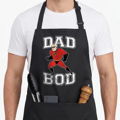 Incredible dad bod apron - Superhero running between DAD and BOD text in red white black — shown on a black cotton canvas apron against a white background