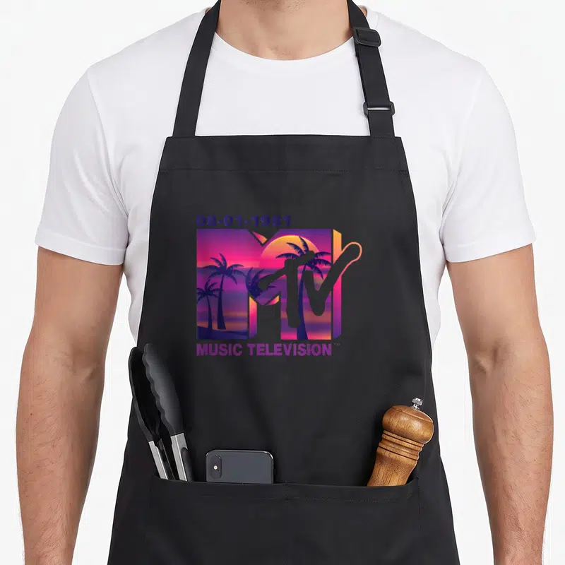Palm mtv apron - 1981 MTV logo with sunset palm trees inside the M and MUSIC TELEVISION text below — shown on a black cotton canvas apron against a white background