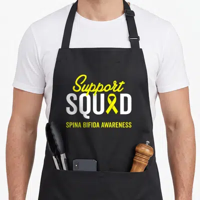 Squad spina bifida awareness apron - Yellow ribbon replaces A in white SQUAD text with Support and Spina Bifida — shown on a black cotton canvas apron against a white background