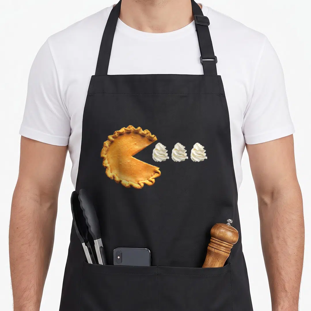 Pie pumpkin apron - Photographic print of pumpkin pie with missing slice and three whipped cream dollops — shown on a black cotton canvas apron against a white background