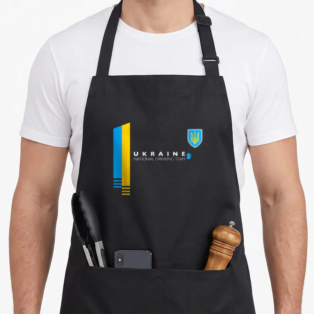 Drinking ukrainian aprons - Stylized blue yellow white flag with UKRAINE NATIONAL DRINKING TEAM text and blue mug icon — shown on a black cotton canvas apron against a white background