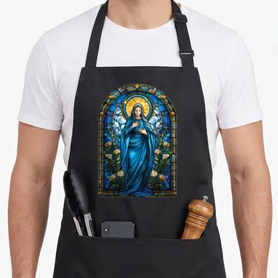 Blessed stained apron - Virgin Mary in blue robes inside arched stained glass window flanked by white roses and gold — shown on a black cotton canvas apron against a white background