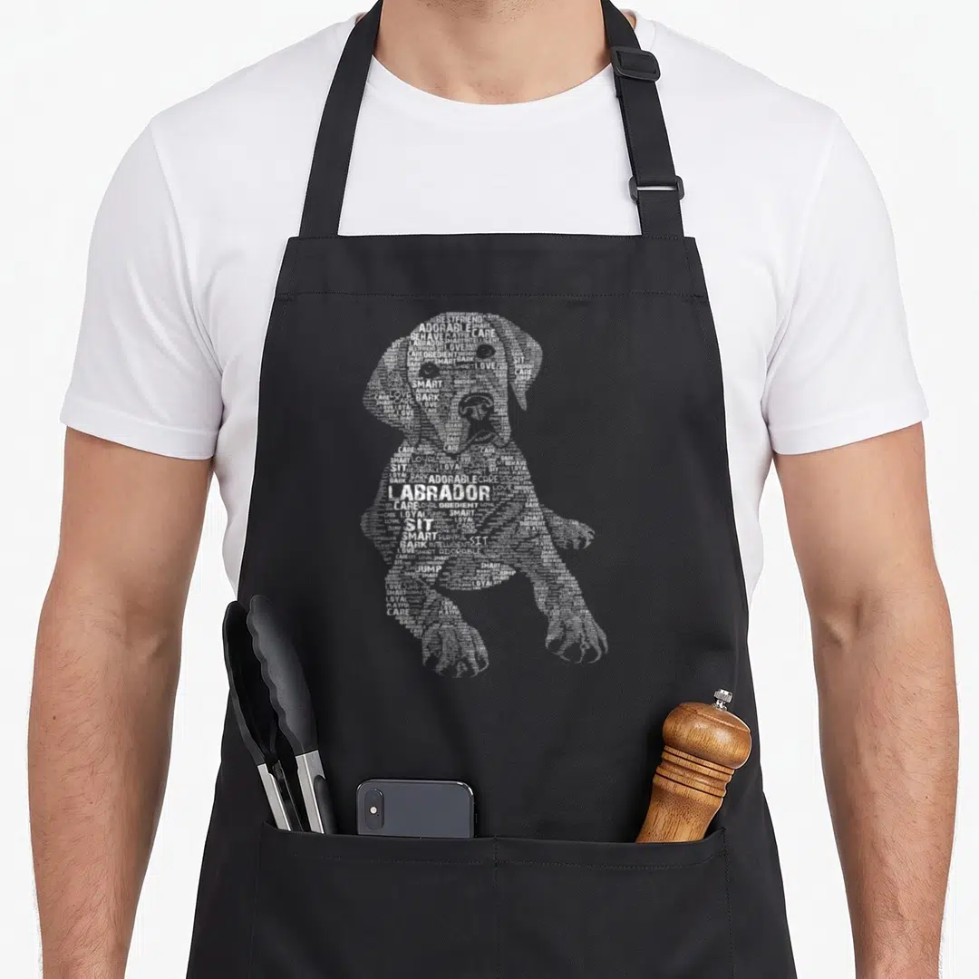 Retriever chocolate labrador apron - White typographic silhouette of a sitting dog with central LABRADOR text — shown on a black cotton canvas apron against a white background