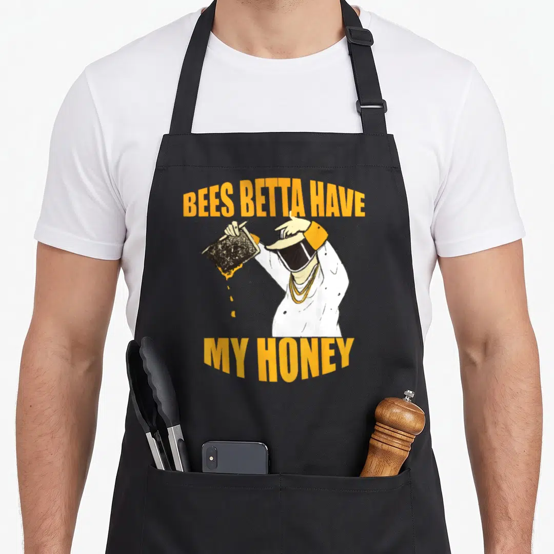 Betta honey bee apron - Cartoon beekeeper holding dripping honeycomb frame with yellow text Bees Betta Have My Honey — shown on a black cotton canvas apron against a white background
