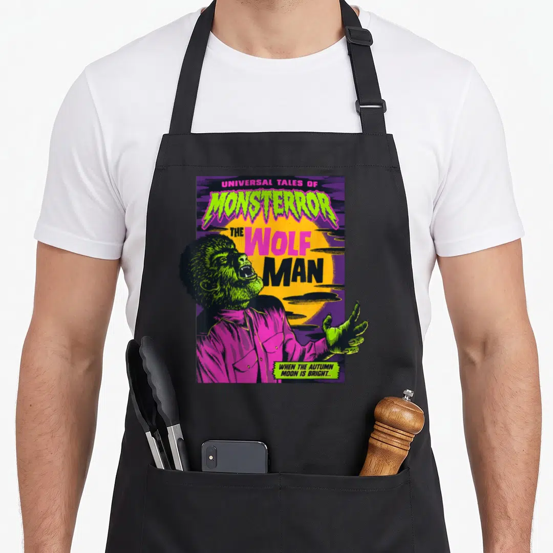 Tale universal monsters apron - Green wolf man in pink shirt against yellow moon with stacked horror text — shown on a black cotton canvas apron against a white background