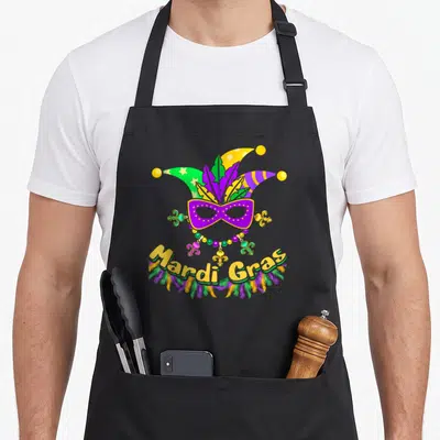 Carnival fat chef apron - Jester hat above purple mask and beads with curved Mardi Gras text — shown on a black cotton canvas apron against a white background