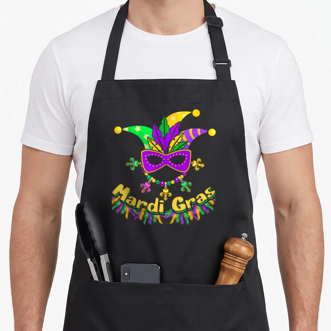 Carnival fat chef apron - Jester hat above purple mask and beads with curved Mardi Gras text — shown on a black cotton canvas apron against a white background