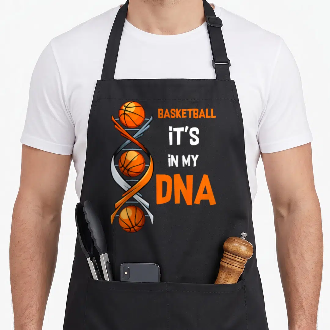 Basketball training apron - Vertical DNA helix with three orange basketballs and stacked text BASKETBALL IT'S iN MY DNA — shown on a black cotton canvas apron against a white background