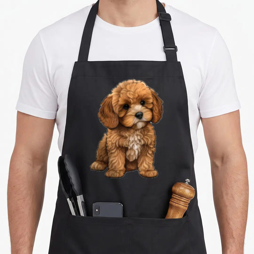 Cavapoo dog breed aprons - Cartoon brown white and black cavapoo puppy sitting centered on canvas — shown on a black cotton canvas apron against a white background
