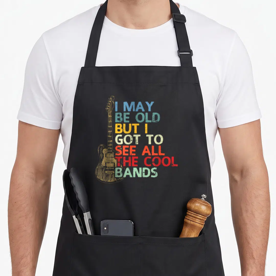 But see may apron - Vintage electric guitar outline next to stacked blue teal yellow red distressed text reading I MAY — shown on a black cotton canvas apron against a white background