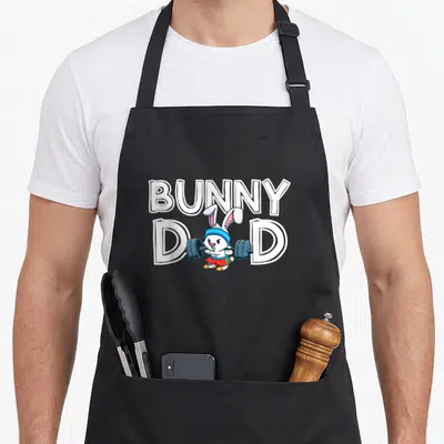 Hare father day apron - Cartoon white bunny lifting grey barbell below BUNNY DAD text in white and blue — shown on a black cotton canvas apron against a white background