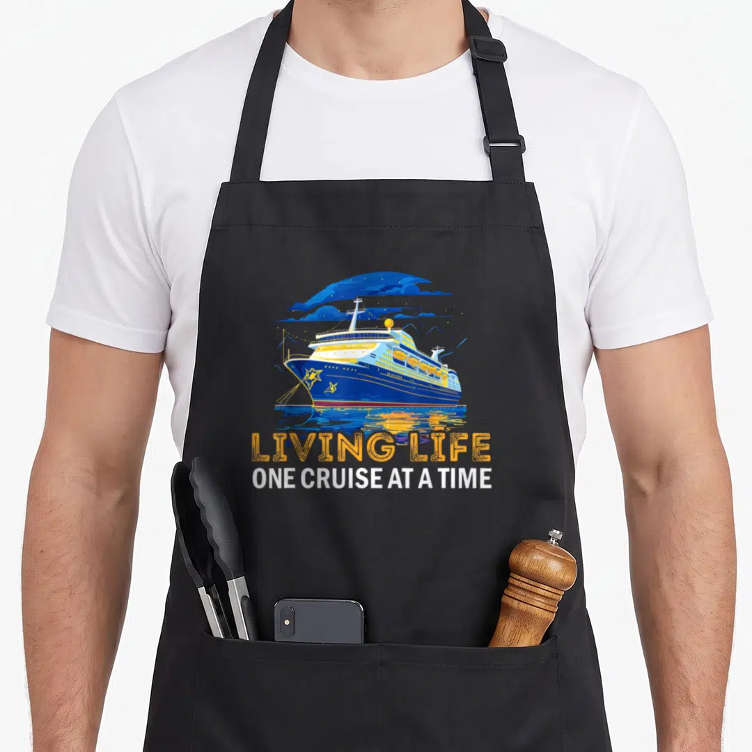 Cruise cruiser apron - Retro blue ship with orange LIVING LIFE and white ONE CRUISE AT A TIME text over water — shown on a black cotton canvas apron against a white background